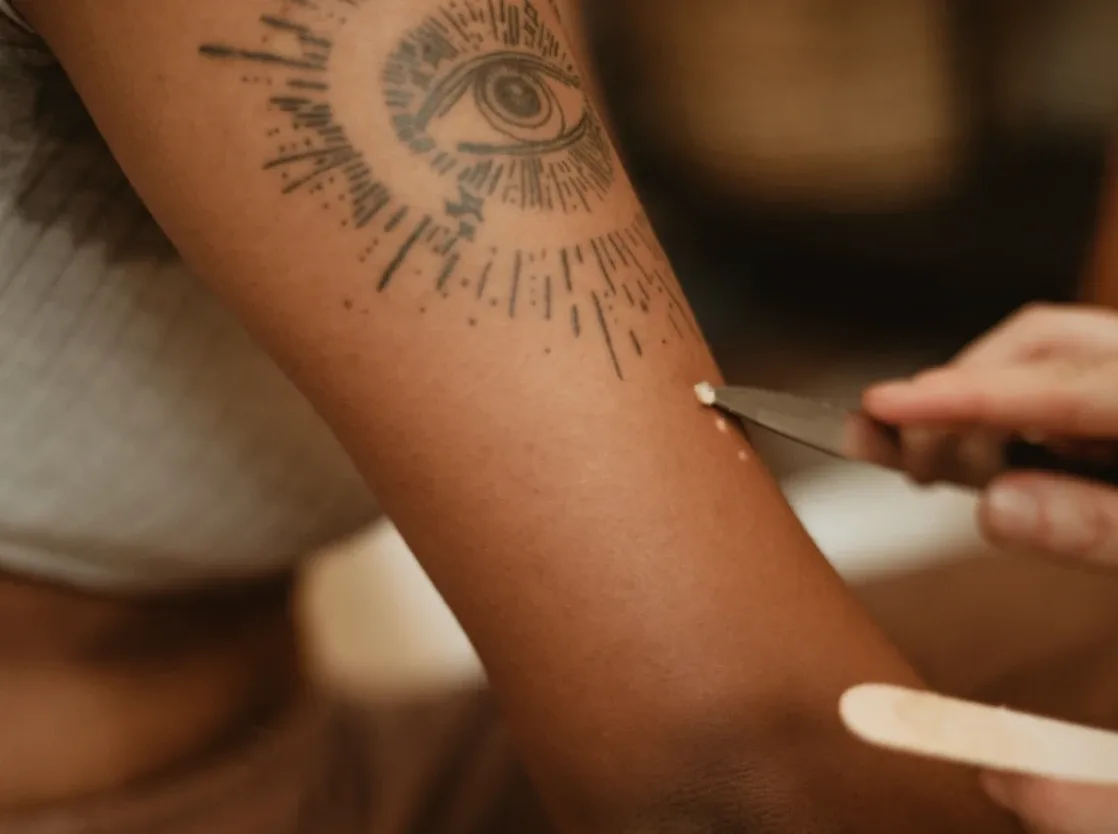 Un avant-bras tatoué d'un œil, une main qui tient un petit outil contre la peau