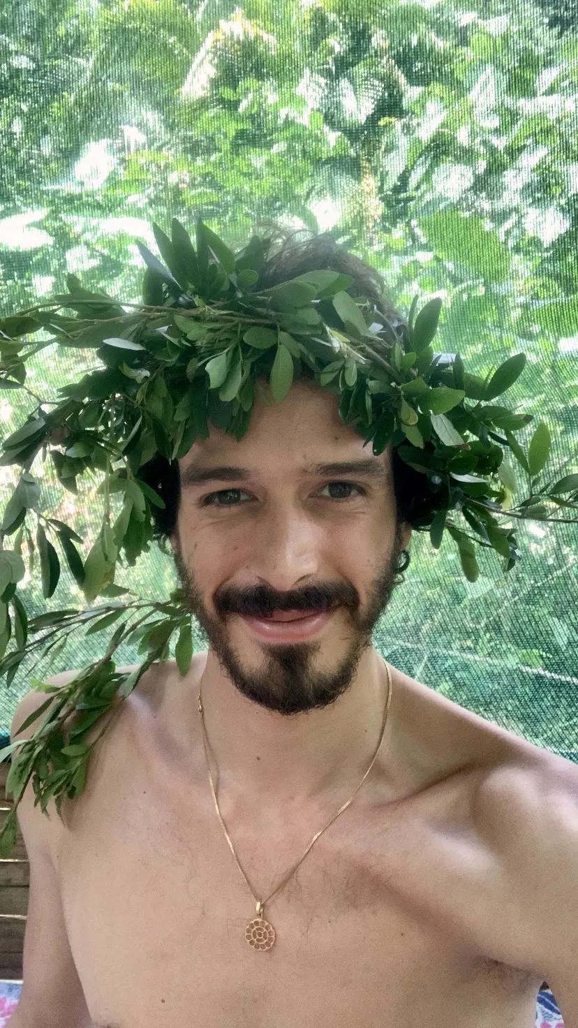 Elliot Amaru smiling, a crown of leaves on his head, in the forest