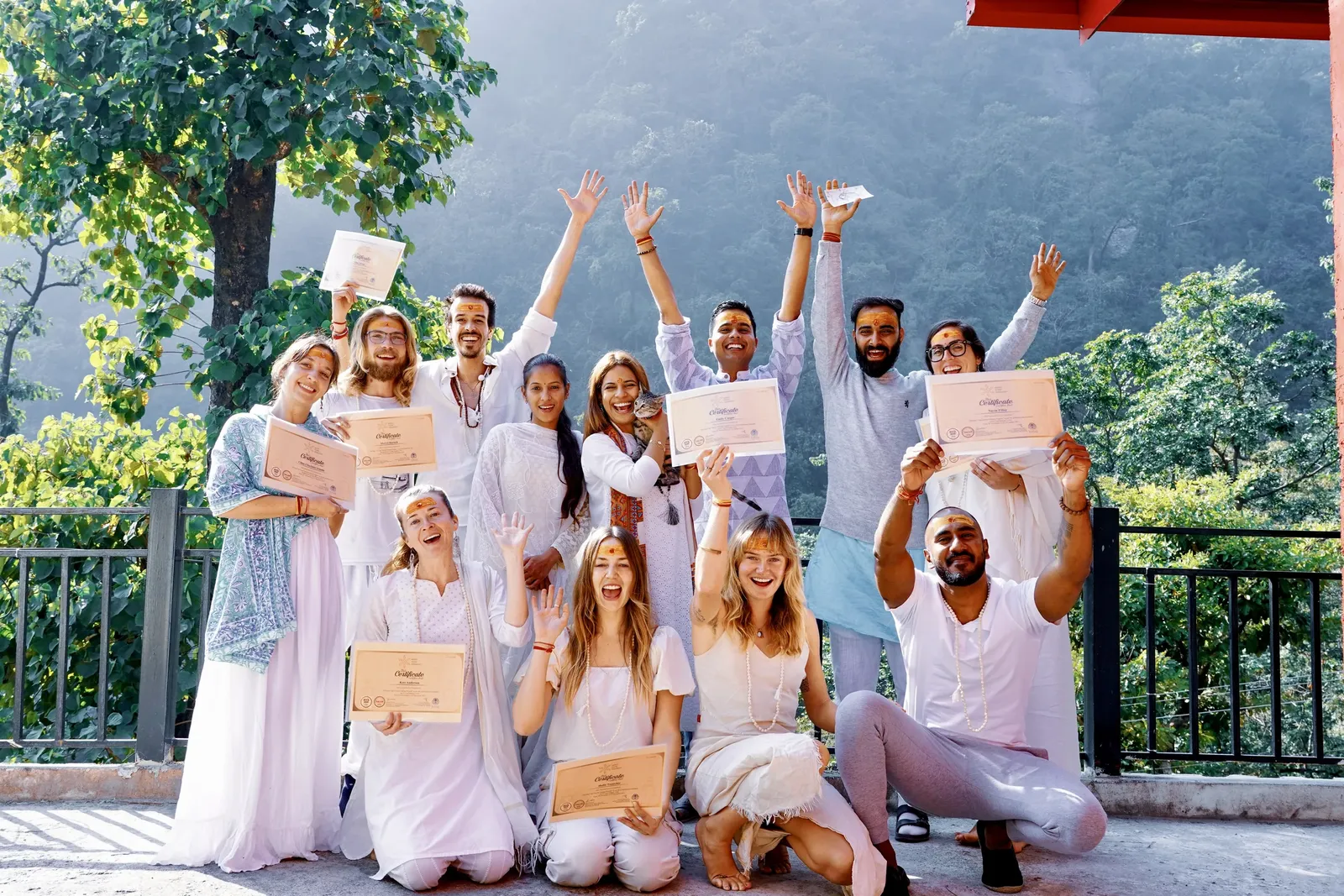 Yoga training graduation: the class in white, certificates in hand, arms raised, in front of the mountains